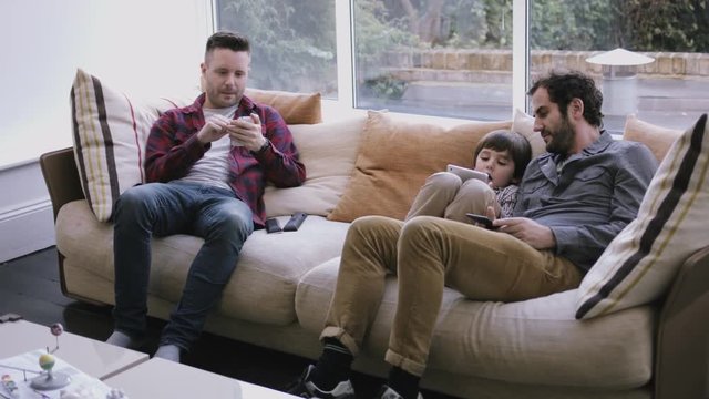 Same Sex Couple Family On The Couch Working With Digital Tablet And Smart Phone