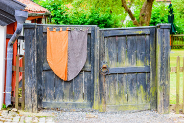 Black old wooden gate with vintage banner. Gate is closed and has a very old locking mechanism and handle.