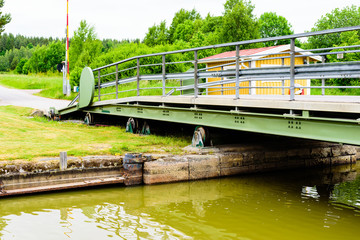 Retractable iron bridge over a canal. Red light signaling boats not to drive through. Bridge is retractable by wheels and rolls to the side when needed.
