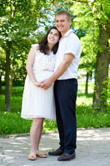 pregnant woman with husband posing in the city park, family portrait, summer season, green grass and trees