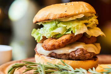 A hamburger consisting of meat patties, lettuce and cheese served on wooden plate