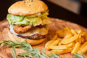 A hamburger consisting of meat patties, lettuce, cheese and French fries served on a wooden plate