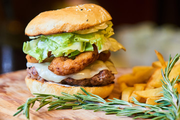 A hamburger consisting of meat patties, lettuce, cheese and French fries served on a wooden plate