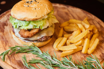 A hamburger consisting of meat patties, lettuce, cheese and French fries served on a wooden plate