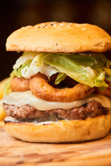A hamburger consisting of meat patties, lettuce and cheese served on wooden plate