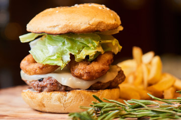 A hamburger consisting of meat patties, lettuce, cheese and French fries served on a wooden plate