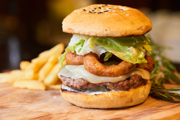 A hamburger consisting of meat patties, lettuce, cheese and French fries served on a wooden plate