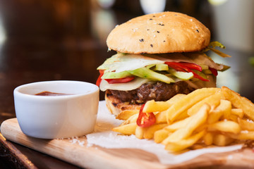 Fast food dinner consisting of hamburger, French fries and a Cup of sauce served on a wooden plate