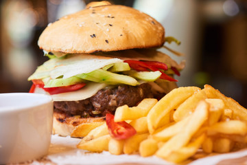 Fast food dinner consisting of hamburger, French fries and a Cup of sauce served on a wooden plate