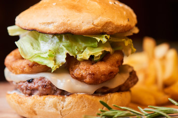 A hamburger consisting of meat patties, lettuce, cheese and French fries served on a wooden plate