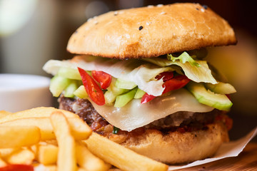 A hamburger consisting of meat patties, cheese, vegetables and French fries closeup