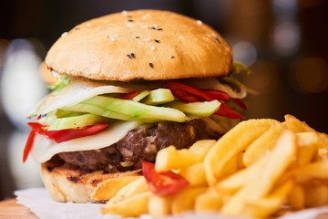 A hamburger consisting of meat patties, vegetables, cheese and French fries closeup
