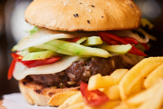 A hamburger consisting of meat patties, vegetables, cheese and French fries closeup