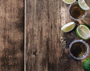Tequila shots with lime slice on dark wooden board, top view