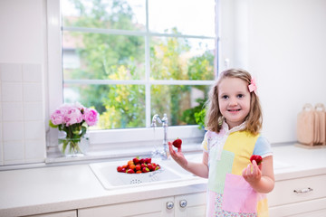 Fototapeta na wymiar Little girl washing strawberries in white kitchen