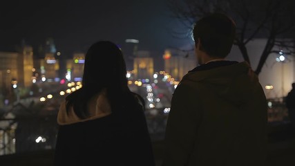 Couple of teenagers looking at night city lights, preparing to run away together