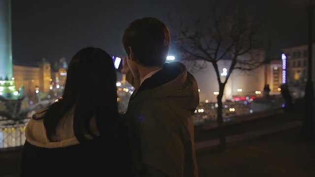 Happy boyfriend and girlfriend taking selfie on smartphone, date in night city