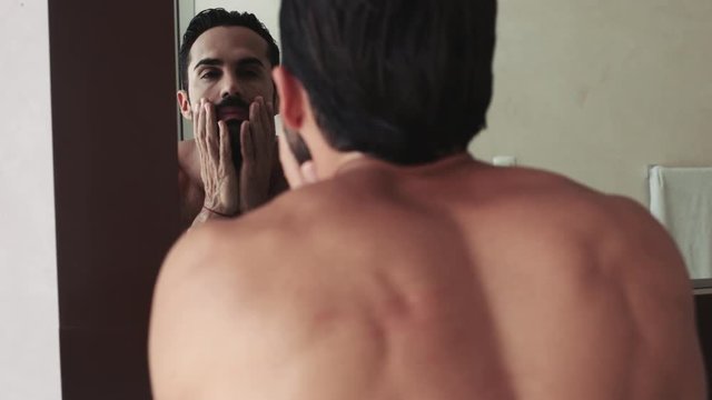 Man washing face and looking into mirror in bathroom