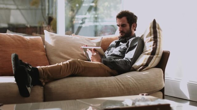 Adult man lying on the couch and using digital tablet