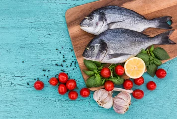 Wall murals Fish Fresh dorado fish on wooden cutting board and vegetables on blue table. Top view, copy space