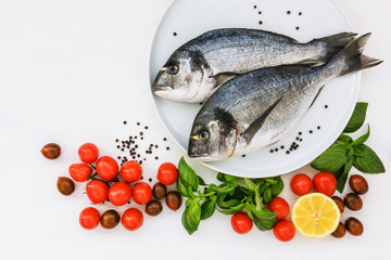 Two fresh dorado fish on white plate and vegetables on white table. Top view, copy space