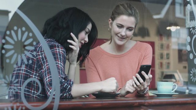 Female friends in coffee shop looking at smart phone