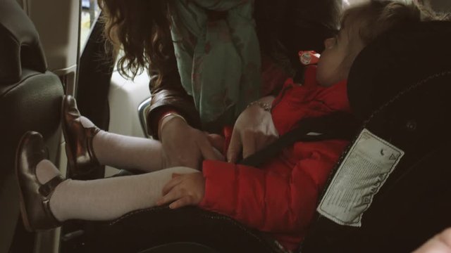 Girl playing harmonica and mother fastening baby girl's seat belt