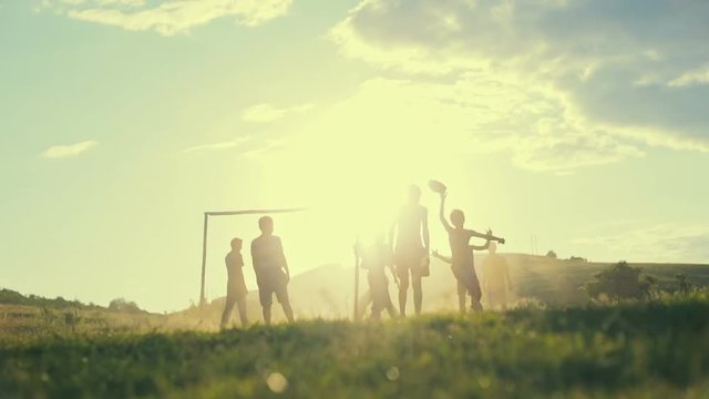 Unidentified children play football in a village on the background of sunset. Slow motion.