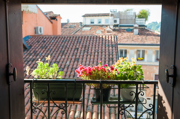 An open window with a typical balcony of northern Italy and some flowered vases © siculodoc