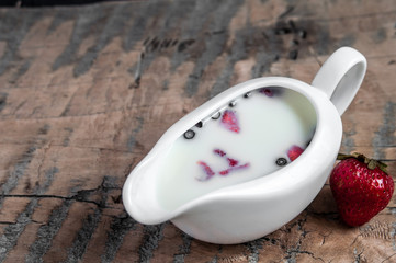 Yogurt with strawberry slices and blueberries on a wooden board - near the yogurt is tasty strawberries