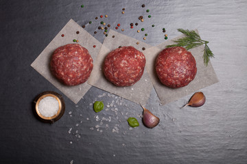 Raw ground beef meat steak cutlets with herbs and spices on blac
