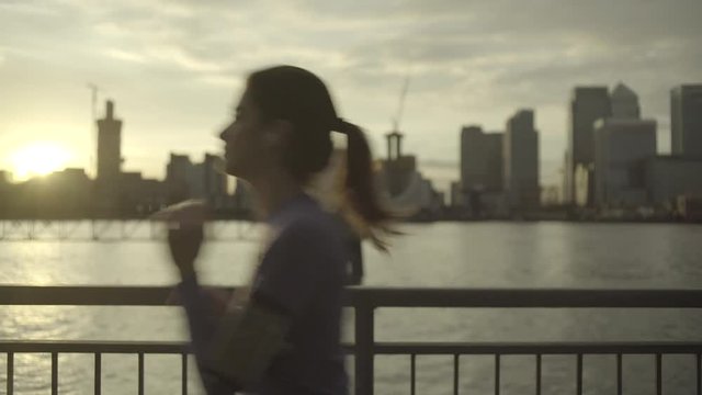 Female runner with headphones jogging by Thames River, London