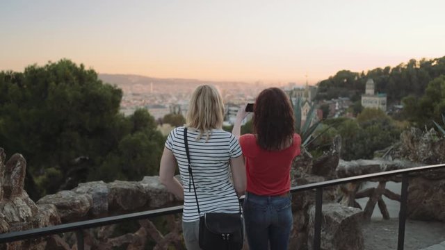 Young adult women admiring view and take picture on mobile phone in Barcelona