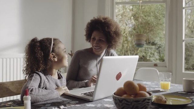 Mother with daughter teaching on laptop in kitchen