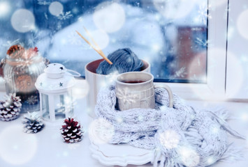 Cup of hot drink in on the windowsill in living room. Comfortable winter weekend or holidays at home. Snow effect