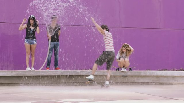 Man spraying water and friends enjoying skateboarding