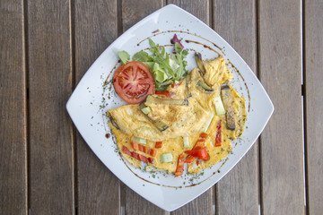 Omlette with herbs,vegetables and cheese in a plate on wooden table.