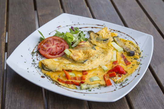 Omlette with herbs,vegetables and cheese in a plate on wooden table.