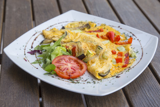 Omlette with herbs,vegetables and cheese in a plate on wooden table.