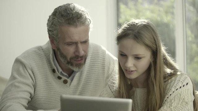Father and teenage child at home looking at digital tablet