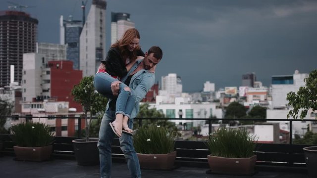 Young man carrying woman on terrace  city in background