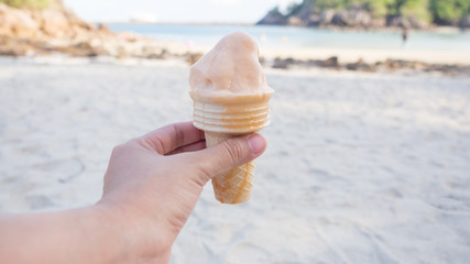 Hand holding icecream cone with nature beach background. Ice cream melting from hot weather.