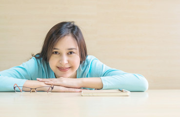 Closeup asian woman lied on desk with happy face in rest time from reading a book on blurred wooden desk and wall textured background in the meeting room , happy time and relaxation of woman concept