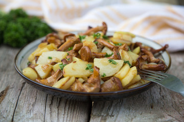 fried young potatoes with chanterelles mushrooms in bowl on old