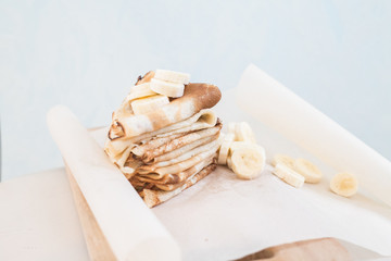 pancakes on parchment with banana. Lunch time. On the table on wooden plank is fried pancakes with banana .