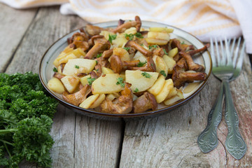 fried young potatoes with chanterelles mushrooms in bowl on old