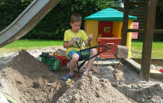 Kind spielt im Sand mit Bagger zur Sommerzeit