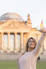 Vain blonde girl with glasses making a selfie. In the background, out of focused Bundestag (Parliament building) of Berlin