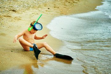little boy posing on the beach wearing snorkeling equipment. On the background of the sea