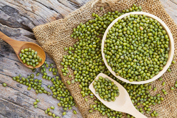 Green bean or mung bean in wooden bowl and spoon with linen fabric sack top view
